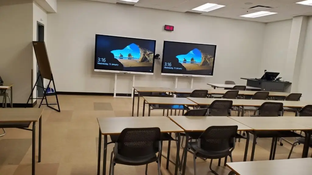 Empty university classroom with desks, chairs, and presentation screens at the front Is this conversation helpful so far?