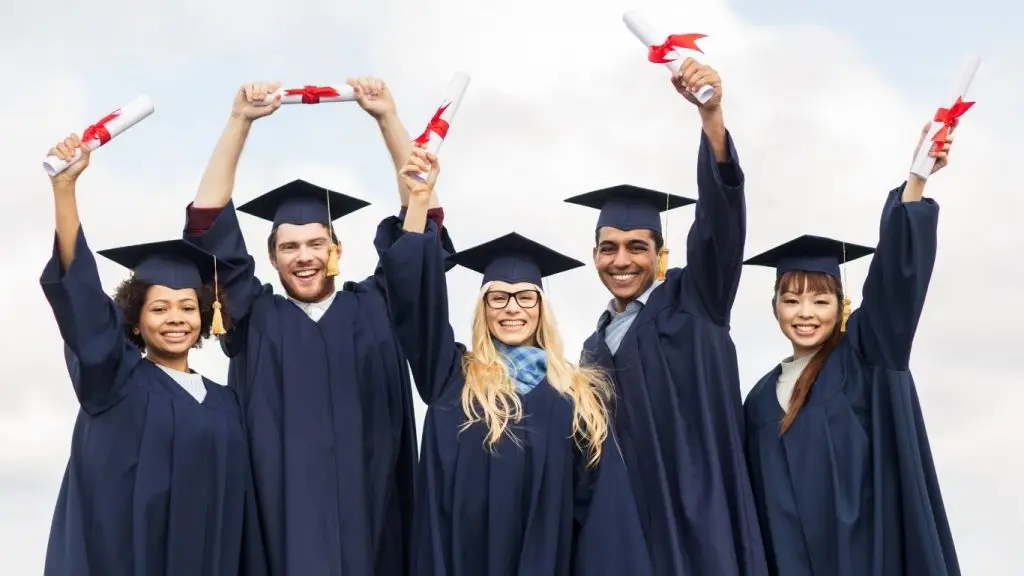 Graduates wearing caps and gowns celebrating while holding diplomas